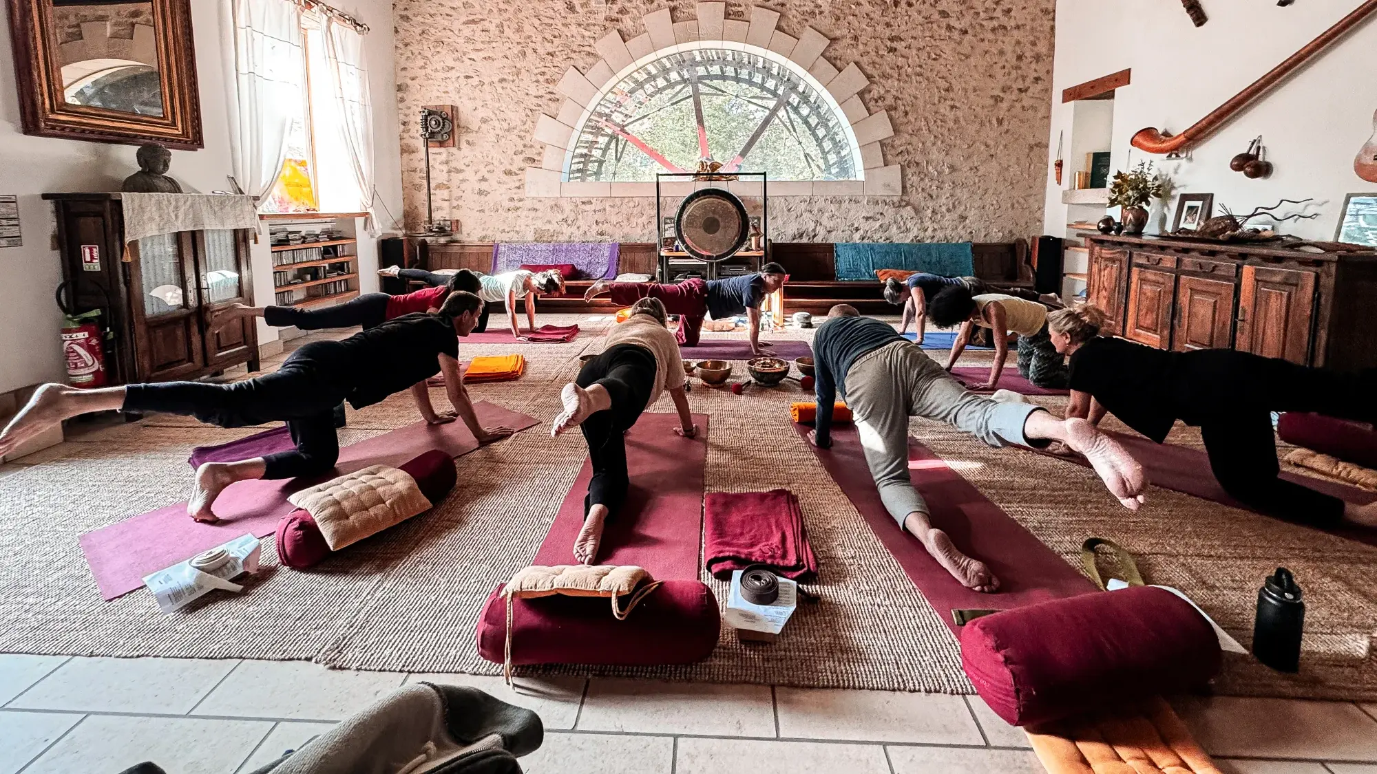 Cours de yoga en groupe guidé par Didier, dans la salle en pierre au gong